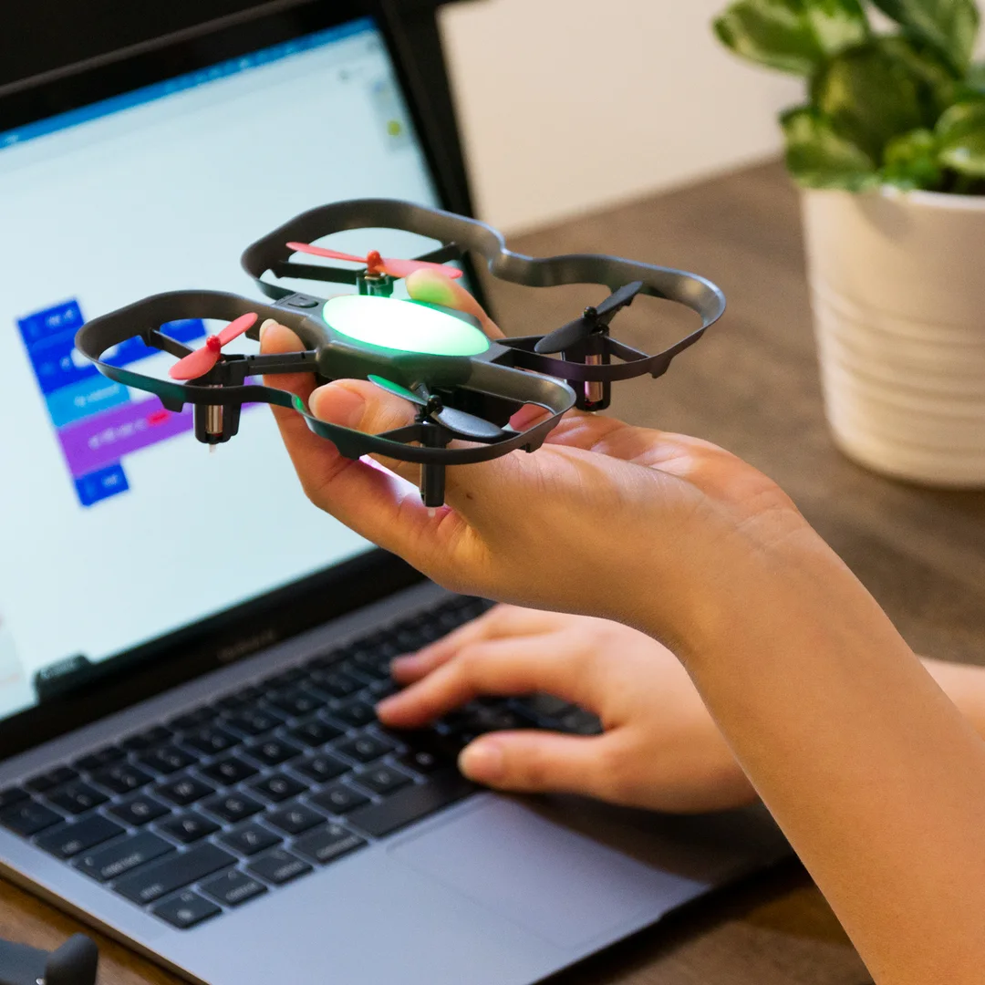 A hand holding a CoDrone EDU in front of a laptop running Blockly