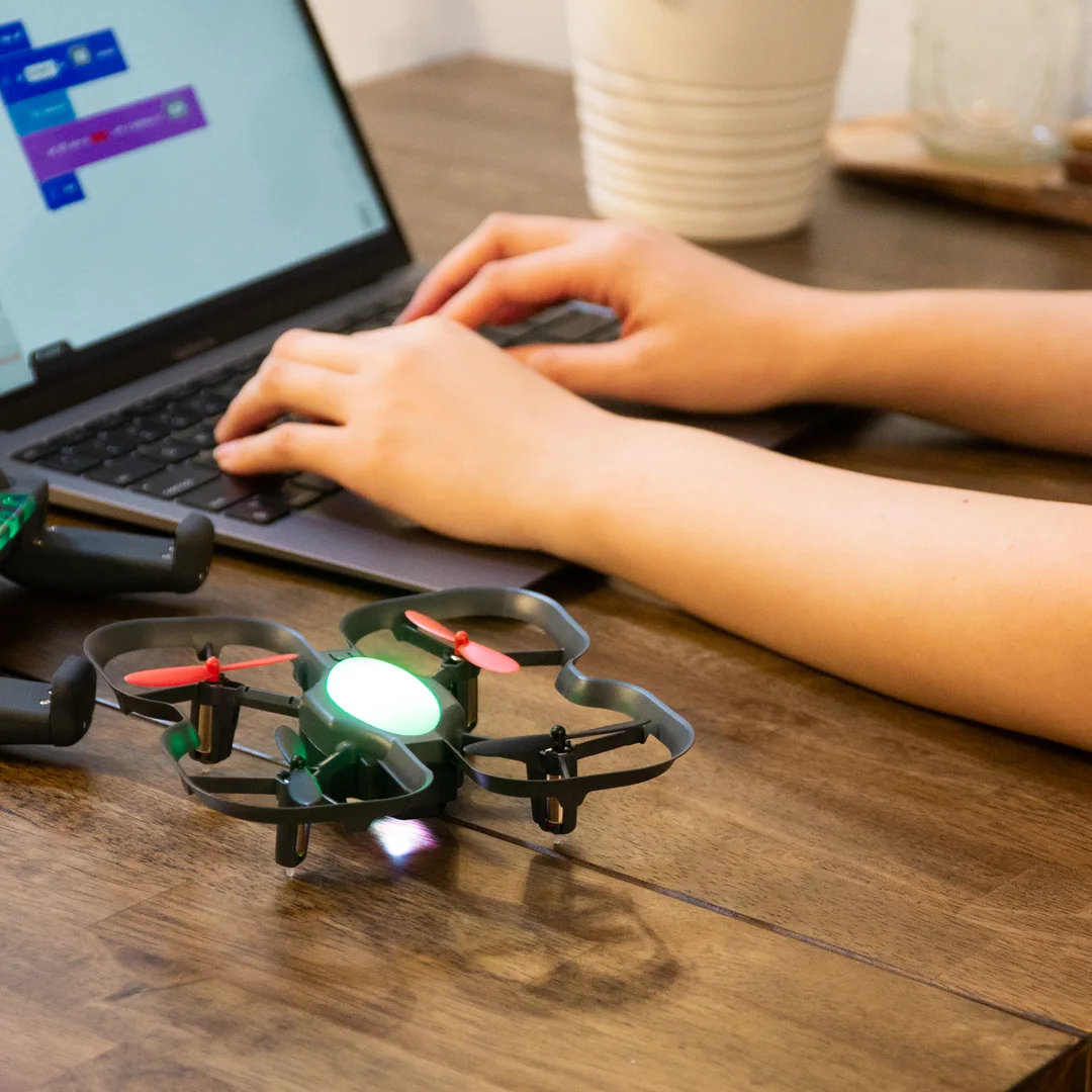 Hands typing Blockly code beside a CoDrone EDU